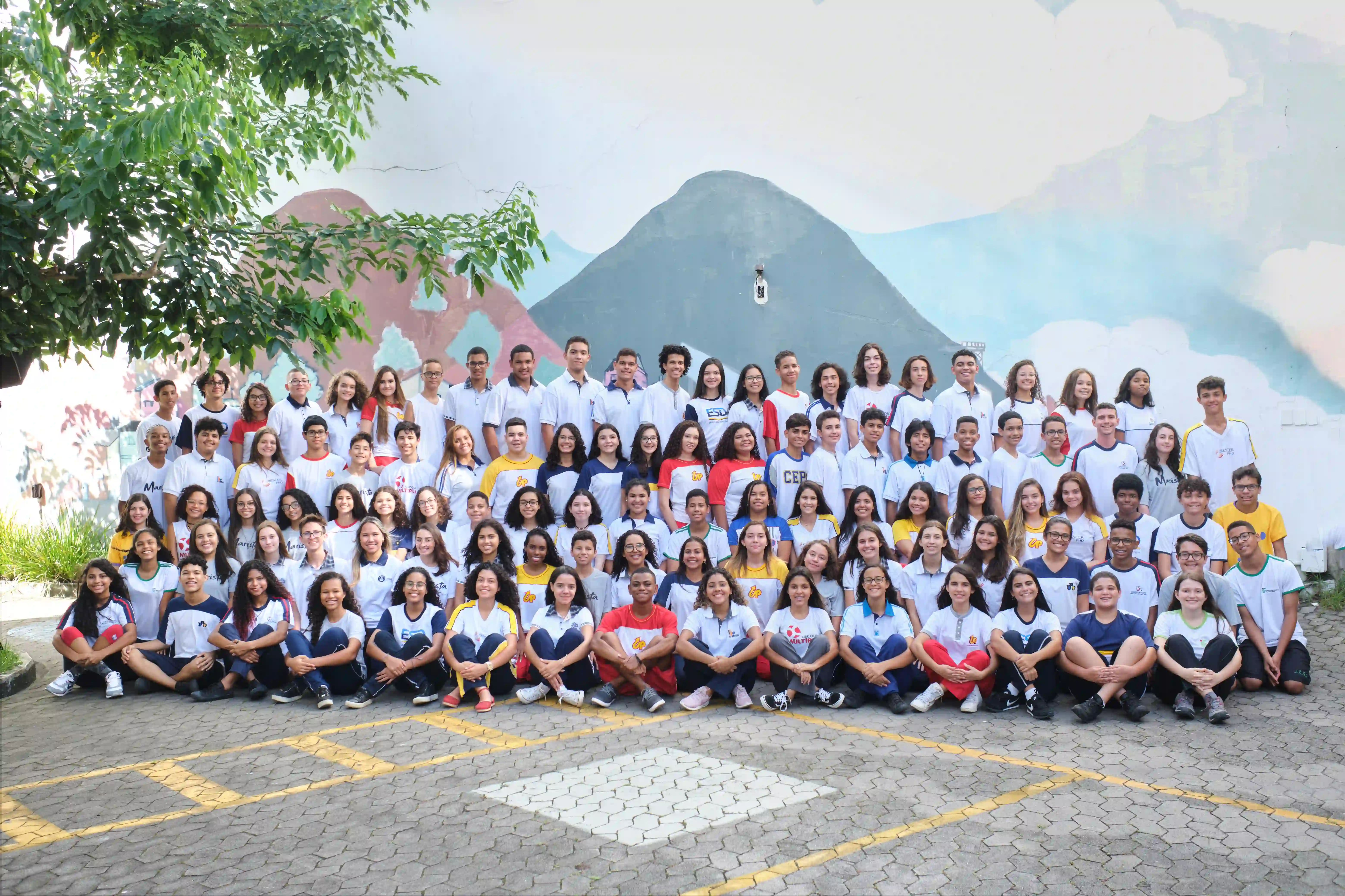 Foto de turma com mais de cem bolsistas do Instituto Ponte, com uniformes de diferentes escolas particulares, diante de um mural
