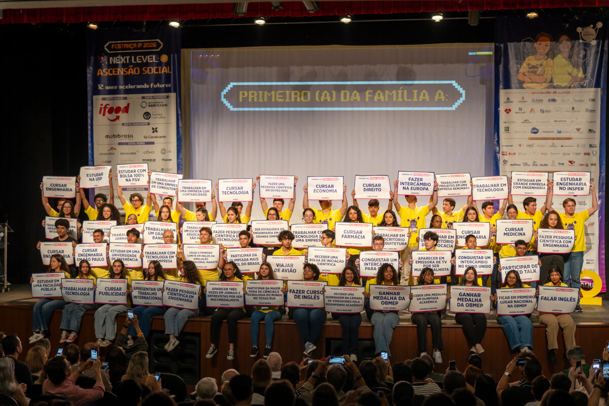 Alunos do Instituto Ponte no palco, com placas que dizem o que serão os primeiros da família a conquistar: cursar engenharia, estudar na USP, fazer intercâmbio