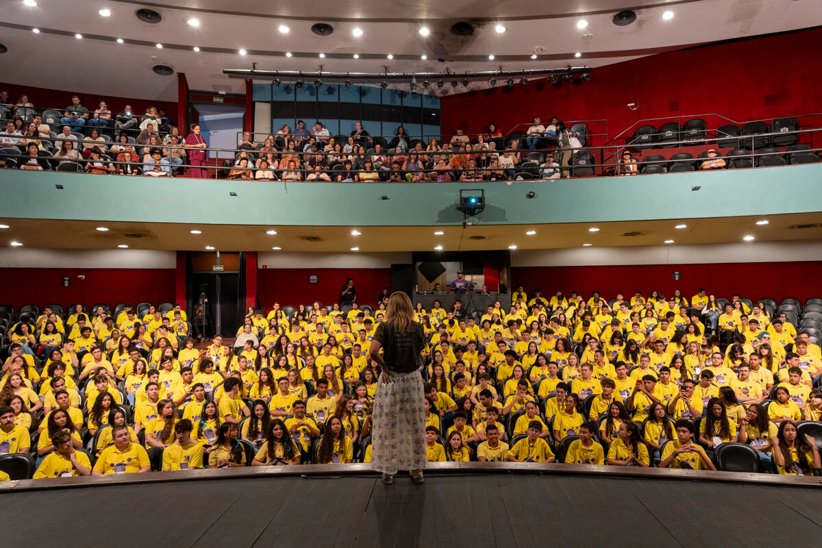 Auditório lotado de alunos do Instituto Ponte, vistos do palco